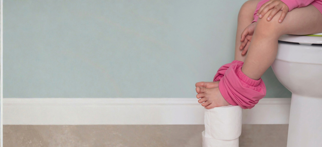 Young child sitting on the toilet during potty training, illustrating constipation and stool withholding in children.